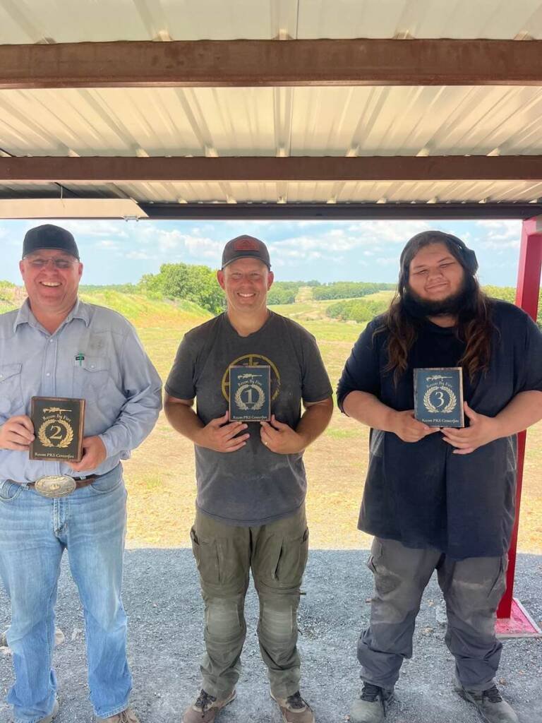Three PRS competition winners smiling with awards under shaded shooting area at Recon By Fire