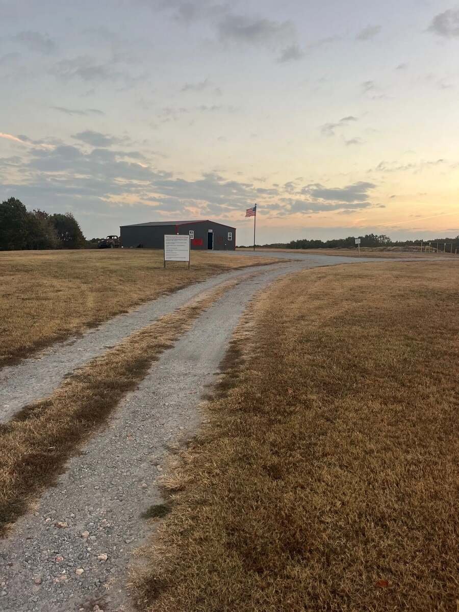 Gravel road leading to Recon By Fire rifle range facility with American flag and sunset sky