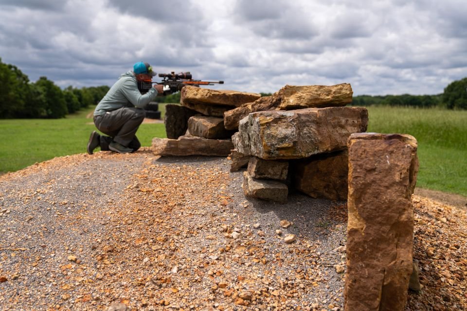 Man aiming rifle while using stacked rocks as shooting support at Recon By Fire Precision Range in Oklahoma